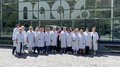 Spunti innovativi per le artigiane dell'Alta Val Pusteria Foto di gruppo di dipendenti con camici bianchi davanti a una grande finestra aziendale