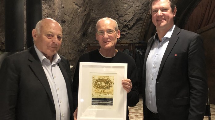 Bilaterale Körperschaft: verdiente Akteure geehrt Drei Männer, einer hält gerahmtes Kunstwerk, stehend in Steinraum