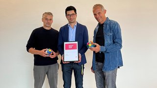 © studiooberhauser Drei Männer halten einen Designpreis und bunte Kugeln in einem hellen Raum
