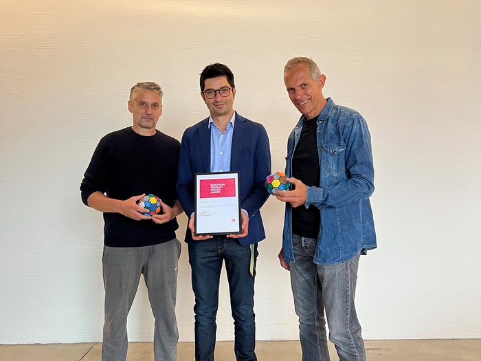 © studiooberhauser Drei Männer halten einen Designpreis und bunte Kugeln in einem hellen Raum