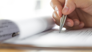 © Shutterstock.com Hand schreibt mit silbernem Stift auf Formular auf Klemmbrett