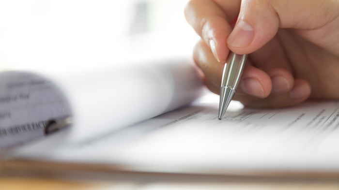 © Shutterstock.com Hand schreibt mit silbernem Stift auf Formular auf Klemmbrett