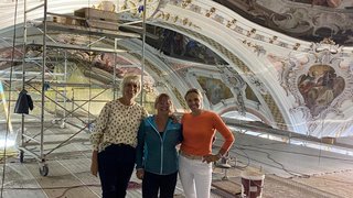 News Drei Frauen stehen in einer restaurierten Kirche mit bemaltem Deckengewölbe und Gerüst
