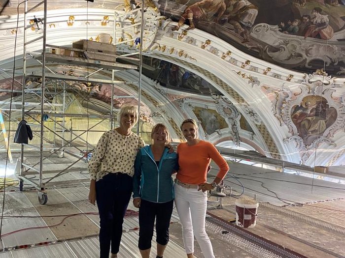 Stuckarbeiten und Fresken in der Pfarrkirche von Toblach Drei Frauen stehen in einer restaurierten Kirche mit bemaltem Deckengewölbe und Gerüst