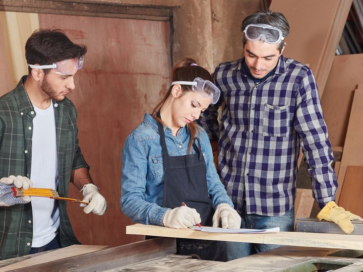 Leistung muss sich lohnen! Drei Handwerker prüfen Pläne und Materialien in einer Werkstatt