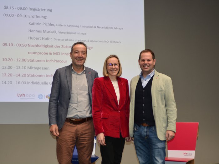 Indirizzare la successione aziendale verso la sostenibilità e la digitalizzazione Tre persone in piedi davanti a uno schermo con programma dell'evento