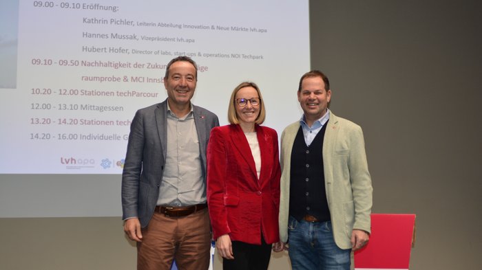 Unternehmensnachfolger/innen auf dem Weg zur Nachhaltigkeit und Digitalisierung begleiten Drei Personen stehen vor einer Leinwand mit Veranstaltungsprogramm