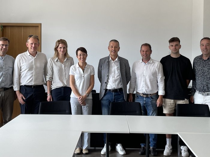 Dreh- und Drohnengenehmigungen in Naturschutzgebieten: Südtiroler Filmproduzenten & Fotografen setzen auf nachhaltige Lösungen Neun Personen in einem Besprechungsraum stehen hinter weißen Tischen