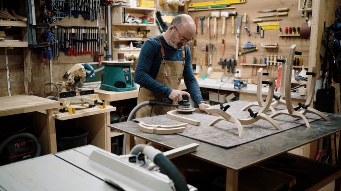 Crowdfunding-Kampagne für nachhaltige Instrumentenständer Tischler schleift Holzstücke in einer Werkstatt mit verschiedenen Werkzeugen