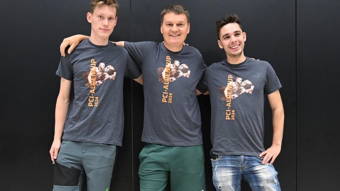 An die Fliese, fertig, los! – Der internationale Wettkampf der Fliesenleger/innen in Bozen Drei junge Männer mit PCI-Alpen Cup 2024 T-Shirts vor schwarzem Hintergrund