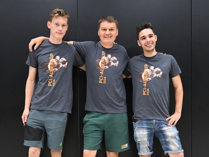 An die Fliese, fertig, los! – Der internationale Wettkampf der Fliesenleger/innen in Bozen Drei junge Männer mit PCI-Alpen Cup 2024 T-Shirts vor schwarzem Hintergrund