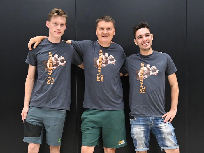 Posata la prima pietra – È partita la competizione internazionale dei piastrellisti a Bolzano! Tre giovani uomini con magliette PCI-Alpen Cup 2024 su sfondo nero