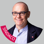 Bolzano periferia Ritratto di uomo sorridente con occhiali su sfondo grigio, banner SINDACO