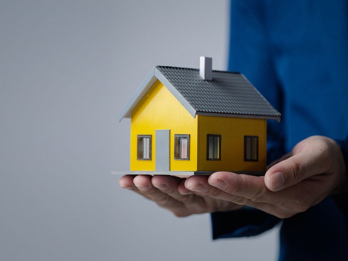 Bauwesen: erste Neuigkeiten und Vereinfachungen im Wohnbau Person hält ein Modellhaus in den Händen vor neutralem Hintergrund