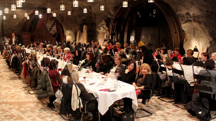 Frauen im Handwerk feiern Jubiläum Viele Personen sitzen bei einem Abendessen in einem festlich beleuchteten Raum mit Steinwänden