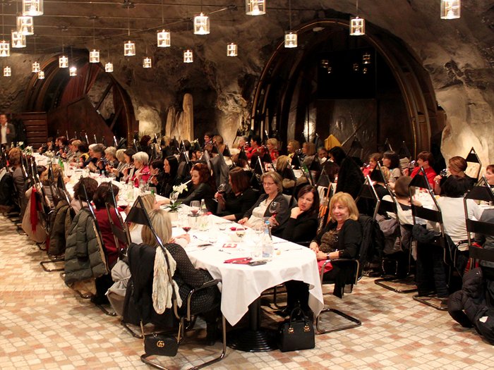 Frauen im Handwerk feiern Jubiläum Viele Personen sitzen bei einem Abendessen in einem festlich beleuchteten Raum mit Steinwänden