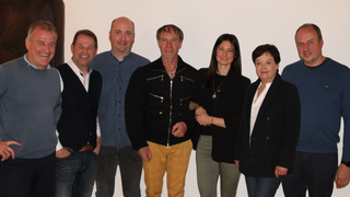 News Gruppe von sieben Personen vor hellem Hintergrund, lächelnd und casual gekleidet