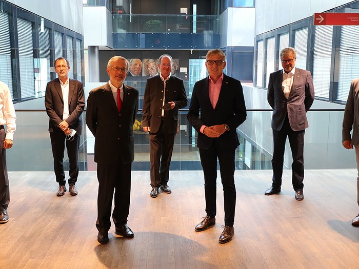 Delegation aus Graz zu Besuch in der Handelskammer Bozen Sieben Männer in Anzügen stehen in einem modernen Bürogebäude