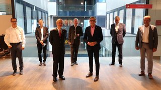 News Sieben Männer in Anzügen stehen in einem modernen Bürogebäude