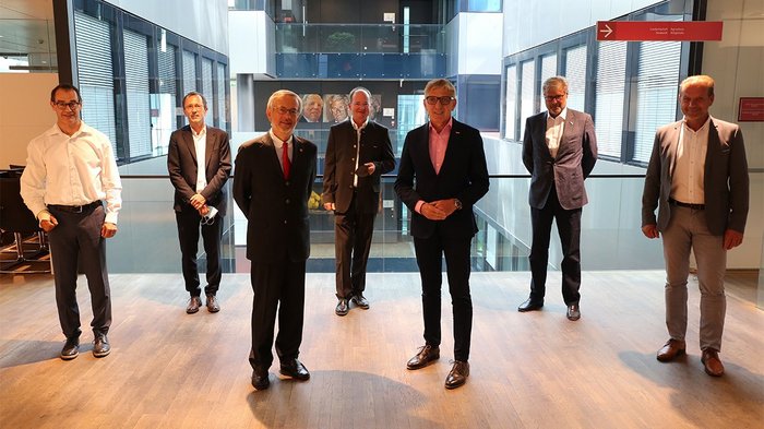 Delegation aus Graz zu Besuch in der Handelskammer Bozen Sieben Männer in Anzügen stehen in einem modernen Bürogebäude