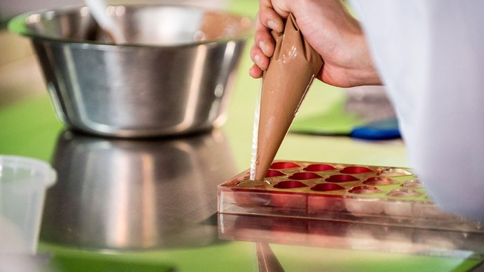 Digitalisierungsschub für Kleinstbetriebe Hand füllt Pralinenform mit flüssiger Schokolade