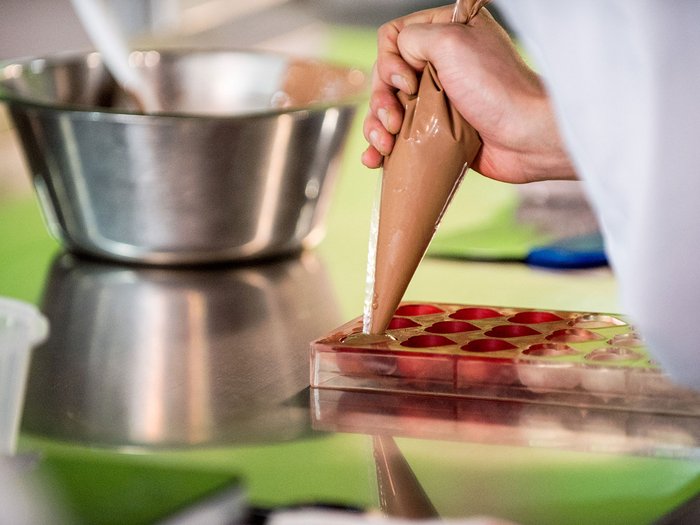 Ostern in Südtirol: Lebensmittelhandwerk überzeugt mit Qualität, Vielfalt und Tradition Hand füllt Pralinenform mit flüssiger Schokolade