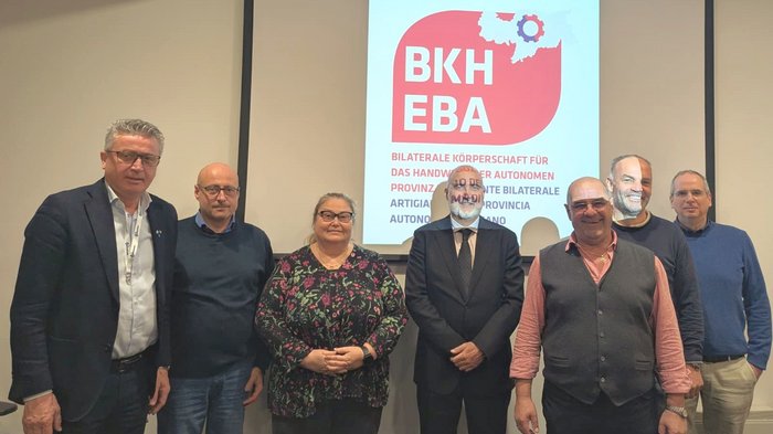 Gemeinschaft und Tradition bei den Dachdeckerinnen und Dachdeckern Sieben Personen posieren vor einer Leinwand mit BKH EBA Logo und Text