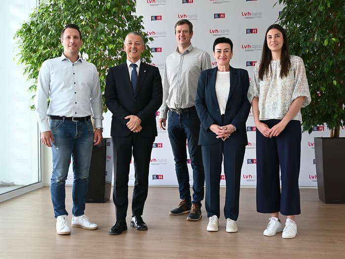 Abitare deve essere accessibile! Sfide e soluzioni in Alto Adige Cinque persone in piedi davanti a muro con loghi LVH APA, sorridenti e formali