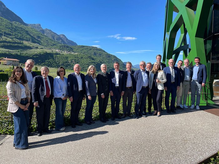 Mut und Miteinander entscheiden die Zukunft Gruppenfoto von 17 Menschen vor Bergen und grünem Gebäude bei sonnigem Wetter