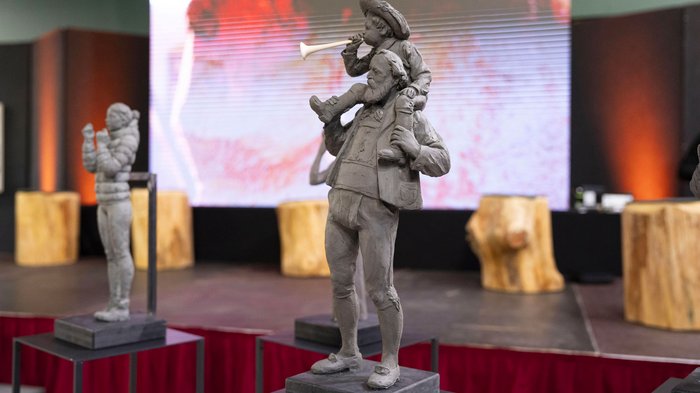 La 31^ Fiera d’Arte UNIKA apre le porte a Ortisei Statua di un uomo con un bambino sulle spalle che suona una trombetta