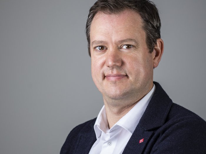 Energiebonus bringt Planungssicherheit Porträt eines lächelnden Mannes in weißem Hemd und dunklem Sakko vor grauem Hintergrund