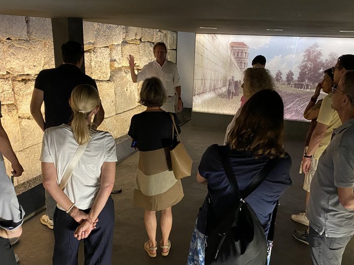 Fünf Länder, ein Ziel: HLS-Techniker/innen setzen auf europäische Zusammenarbeit Gruppe hört auf eine Führung vor antiker Mauer und Wandprojektion