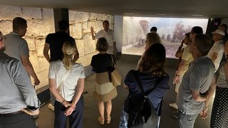 News Gruppe hört auf eine Führung vor antiker Mauer und Wandprojektion