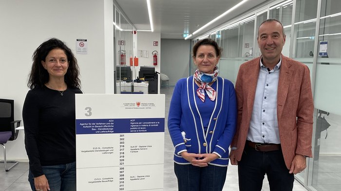 Treffen AOV Drei Personen stehen in einem Büro neben einem Schild mit Behördeninformationen