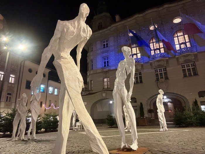 Kunst auf dem Rathausplatz – und ein Gespräch darüber, was sie auslöst Weiß gestrichene abstrakte menschliche Skulpturen vor einem beleuchteten Gebäude bei Nacht