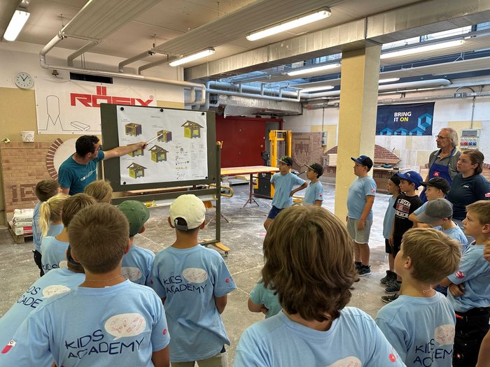 Kids-Academy 2024: Eine lehrreiche Erfahrung im Vinschgau Kinder in blauen T-Shirts erhalten Bauanleitung von Lehrer in Werkstatt