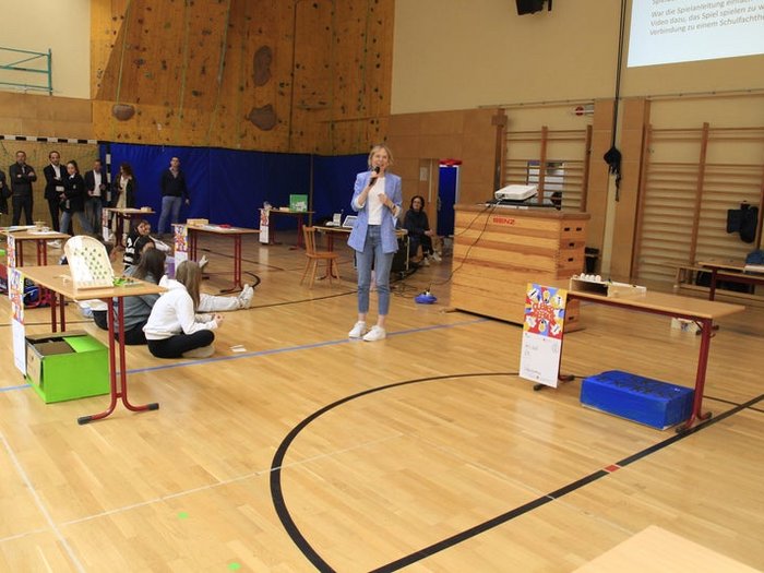 Kreative Spielideen: Preisverleihung für "Clever gebaut" Frau spricht in Sporthalle vor sitzenden und stehenden Zuhörern