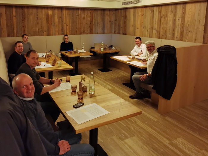 Costruttori e Muratori: “I prezzi di riferimento devono essere più sostenibili!” Gruppo di otto persone in riunione attorno a tavoli di legno in ambiente accogliente