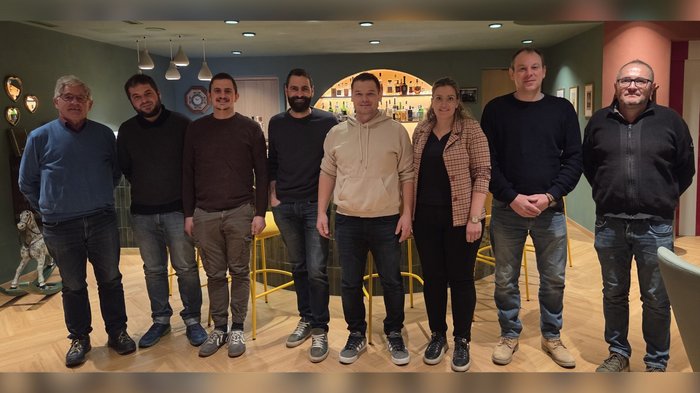 Haller: „Reine Versprechen, sonst nichts!“ Acht Personen stehen nebeneinander in einem Zimmer mit Bar im Hintergrund