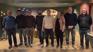 News Acht Personen stehen nebeneinander in einem Zimmer mit Bar im Hintergrund