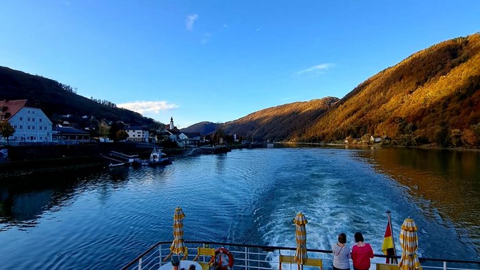 Auf Reisen: Althandwerker auf Flusskreuzfahrt Blick von einem Boot auf einen Fluss mit Hügeln und Sitzbereichen auf dem Deck
