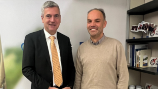 News Zwei Männer in Büro, einer im Anzug, der andere in Pullover, lächelnd