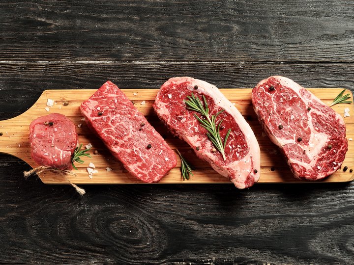 Metzger Verschiedene rohe Rindfleischsteaks mit Rosmarin auf Holzbrett