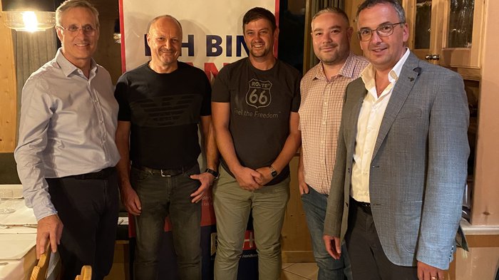 Neuer Handwerkerobmann in Schluderns Fünf Männer stehen in einem Holzraum vor einem Banner mit freundlichen Gesichtern