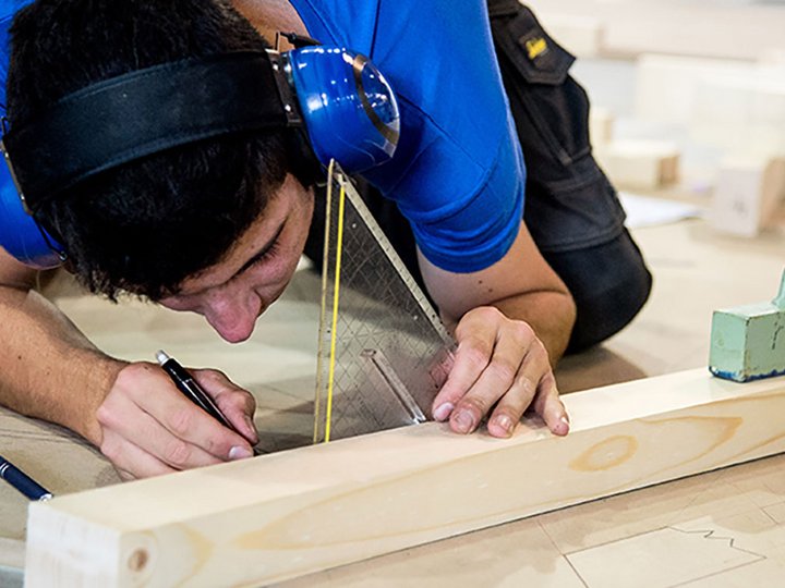 Formazione professionale Artigiano misura e segna una tavola di legno con protezioni acustiche