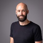 Christian Höppe Ritratto di uomo sorridente con barba e maglietta nera su sfondo grigio