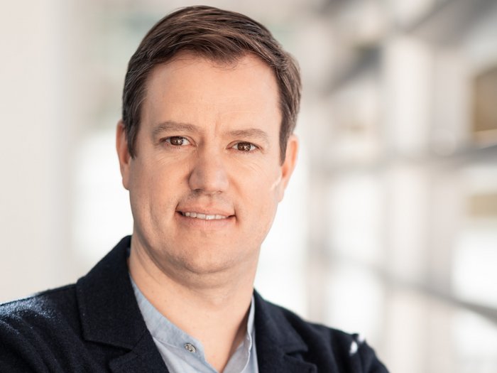 Mietwagenunternehmer: Nur staatliche Lösungen sind effizient! Porträt eines Mannes mit verschränkten Armen in einem modernen Büro