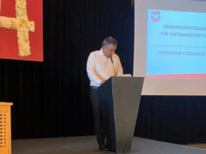 E-Mobilität: lvh-Mietwagenunternehmer schauen in die Zukunft Mann hält Vortrag auf Bühne neben Präsentationsfolie mit kommunaler Verordnung