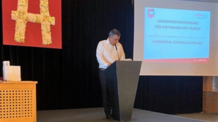 E-Mobilität: lvh-Mietwagenunternehmer schauen in die Zukunft Mann hält Vortrag auf Bühne neben Präsentationsfolie mit kommunaler Verordnung