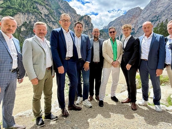 Fünf Länder, eine Branche, viele gemeinsame Herausforderungen Neun Männer in Anzügen stehen vor einem Bergsee und Felsen im Hintergrund